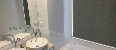 A bathroom with two sinks, a mirror, and a bathtub.
