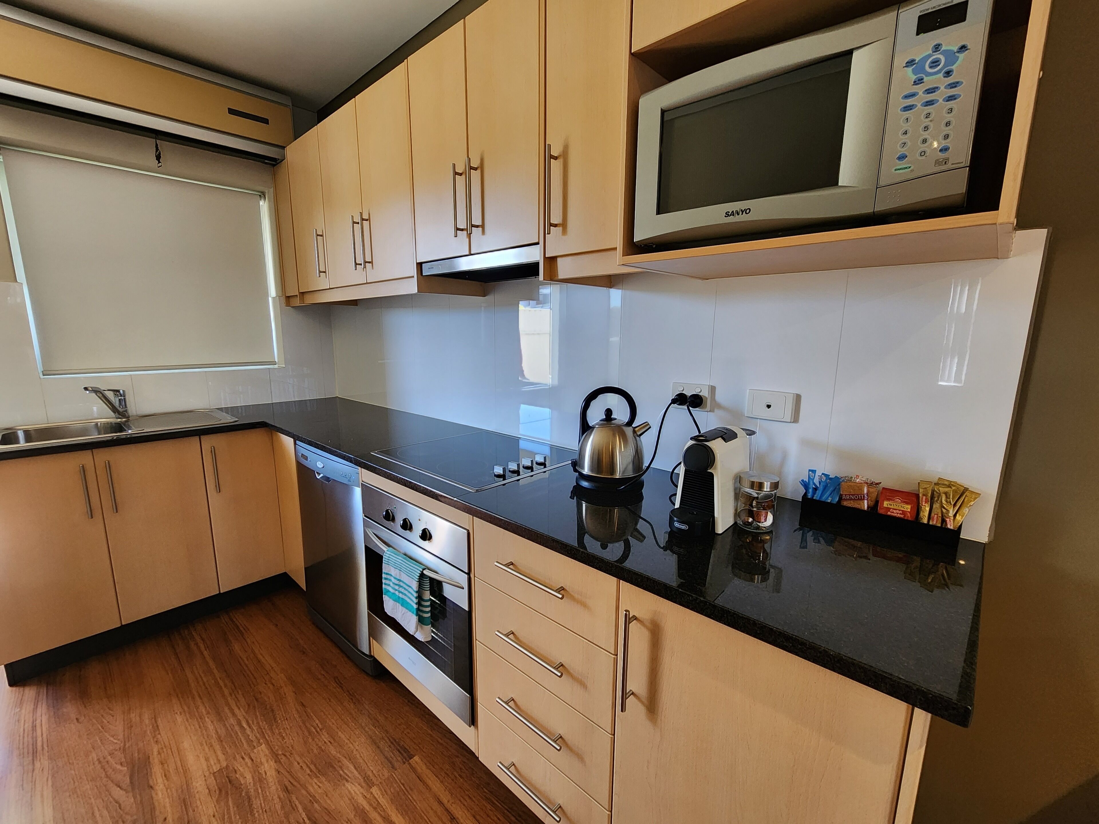 Una cocina moderna con armarios de madera, un horno de acero inoxidable, un microondas y un hervidor sobre la encimera.