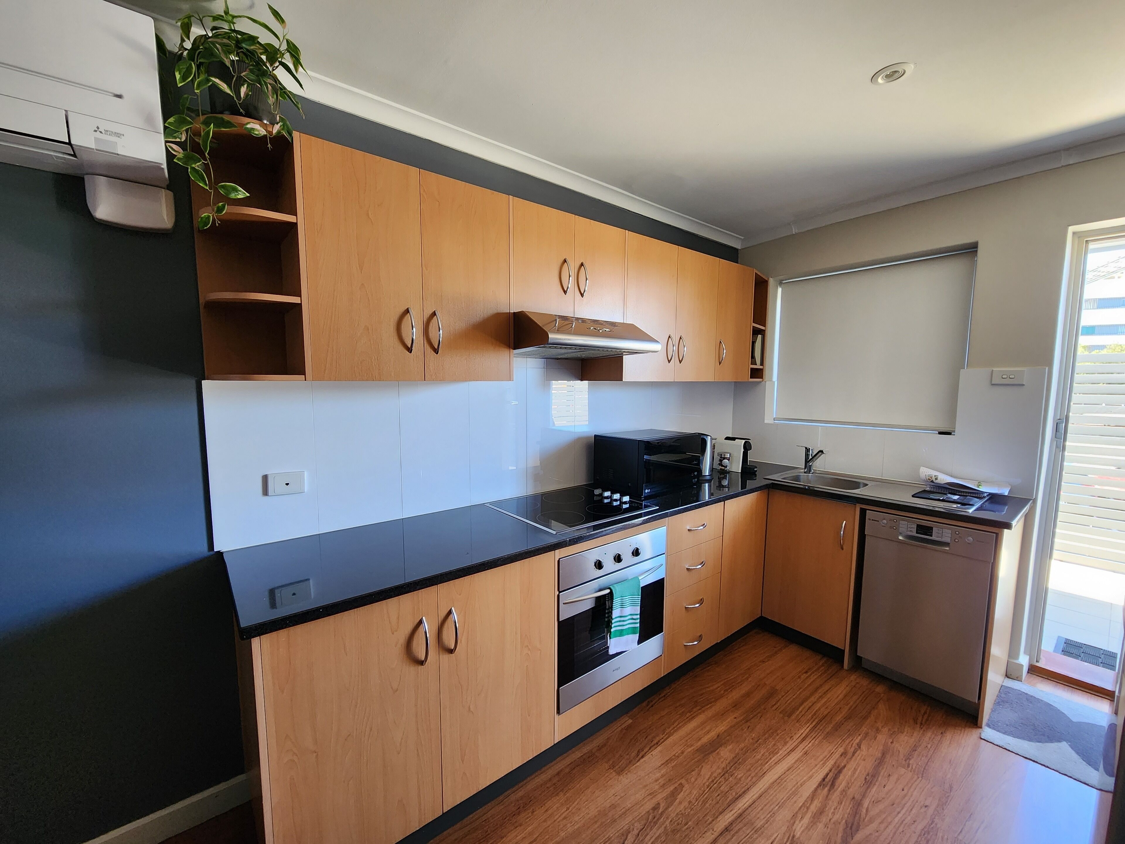 A modern kitchen with wooden cabinets, a black countertop, stainless steel appliances, and a window with blinds.