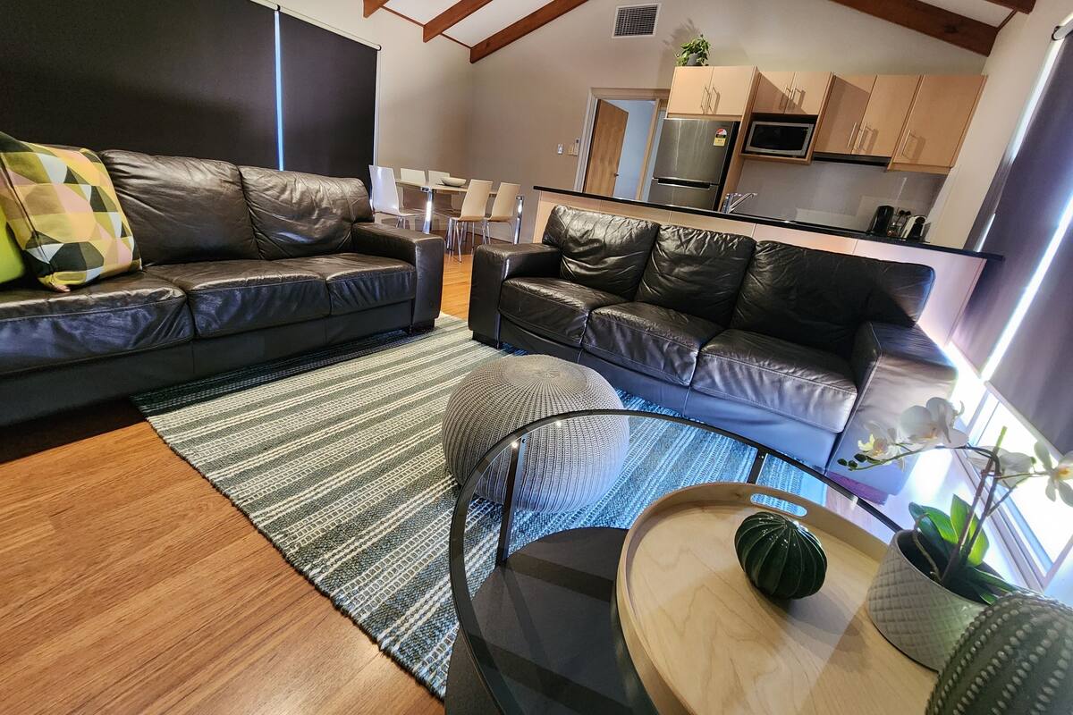 A modern living room with two black leather sofas, a glass coffee table, and a striped rug.