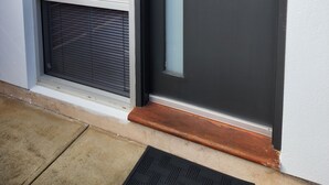 Uma porta moderna com fechadura eletrônica, uma porta de vidro deslizante e um pequeno degrau que leva à entrada.
