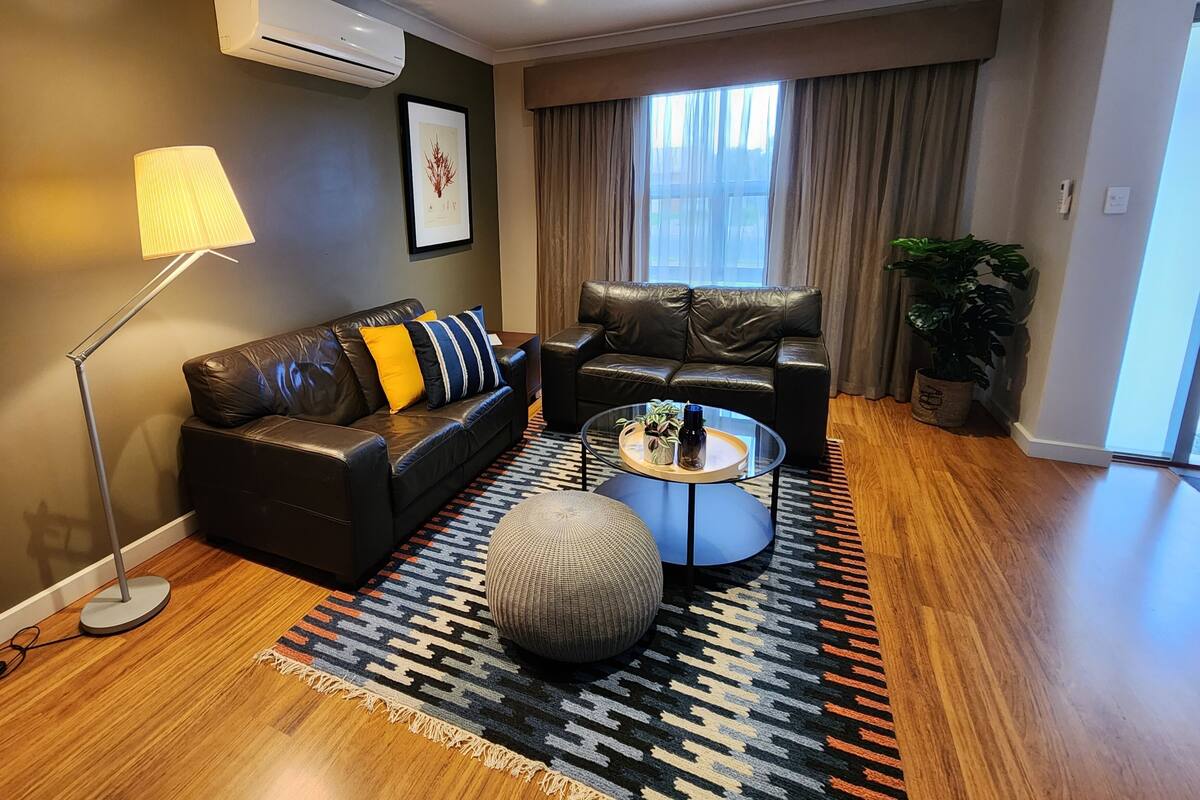 A modern living room with a leather sofa, a round coffee table, a floor lamp, and a patterned rug.