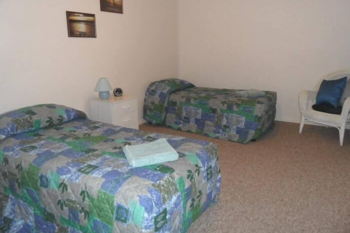 A room with two beds, a chair, a nightstand, and a lamp.