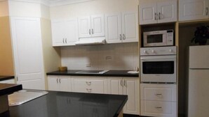 A kitchen with white cabinets, a black countertop, a microwave, an oven, and a refrigerator. - Sylvan Beach Resort (Bellara)