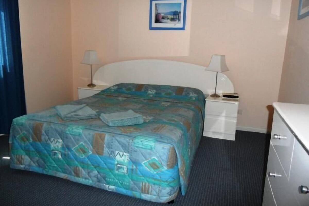 A hotel room with a bed, two bedside tables, a lamp on each table, a picture on the wall, and a dresser.