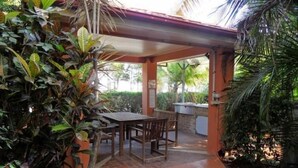 An outdoor patio area with a table and chairs, surrounded by lush greenery and a covered seating area. - Sylvan Beach Resort (Bellara)
