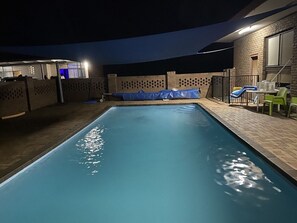 A swimming pool with a blue tarp covering part of it, surrounded by a brick wall and a covered seating area with chairs. - Charlton Motel - Victoria (Charlton)