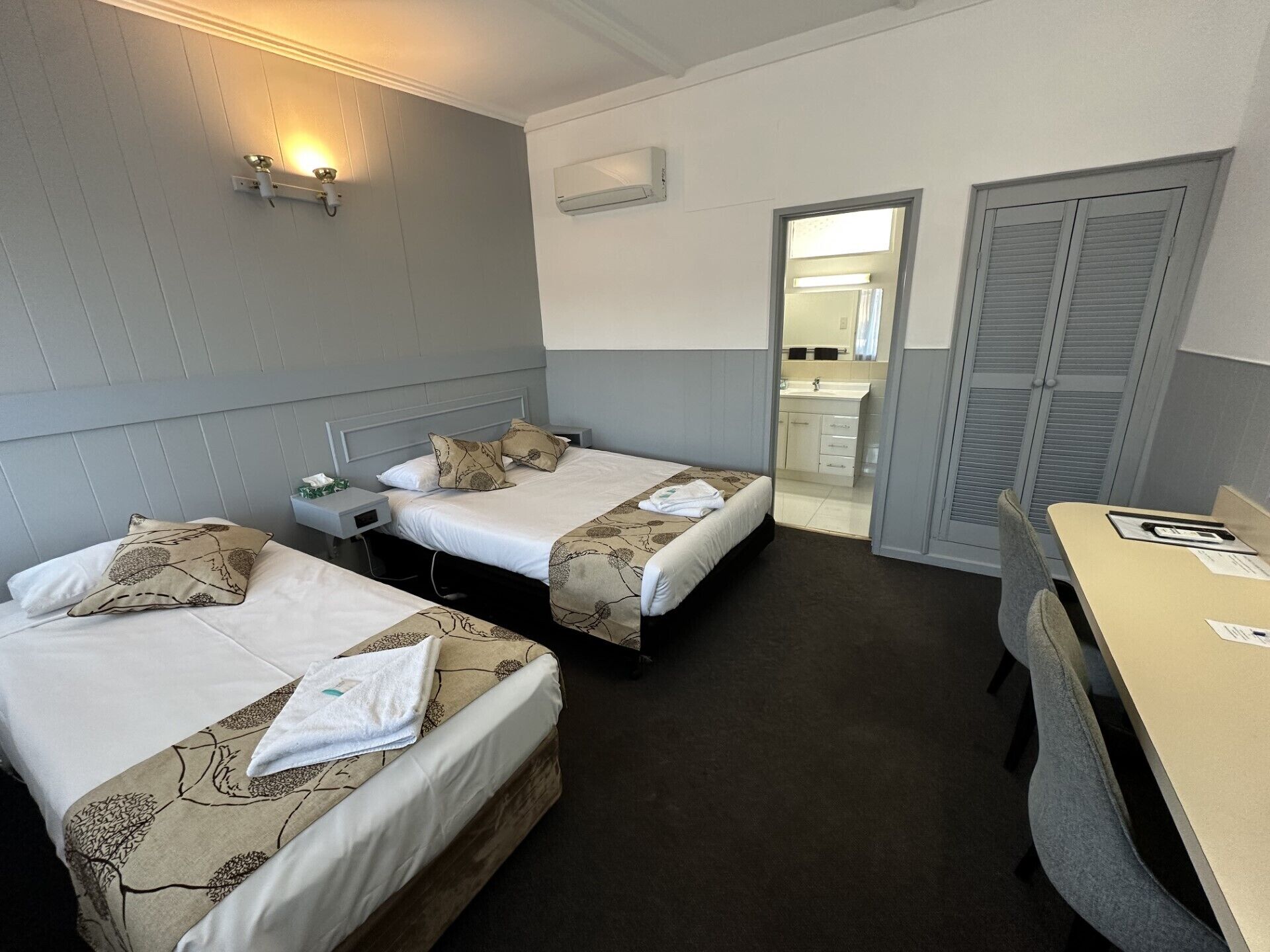 A hotel room with two single beds, a desk, and a bathroom visible through an open door.