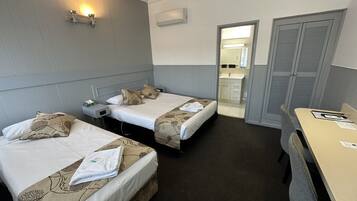 A hotel room with two single beds, a desk, and a bathroom visible through an open door.