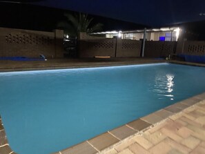 A swimming pool at night with a brick wall and a covered area in the background. - Charlton Motel - Victoria (Charlton)