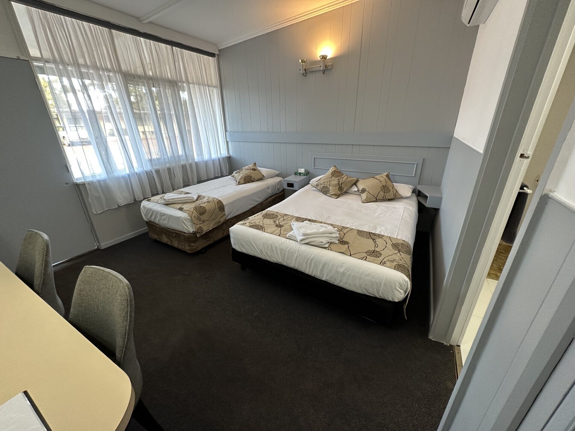 A hotel room with two beds, a small table, and a chair.