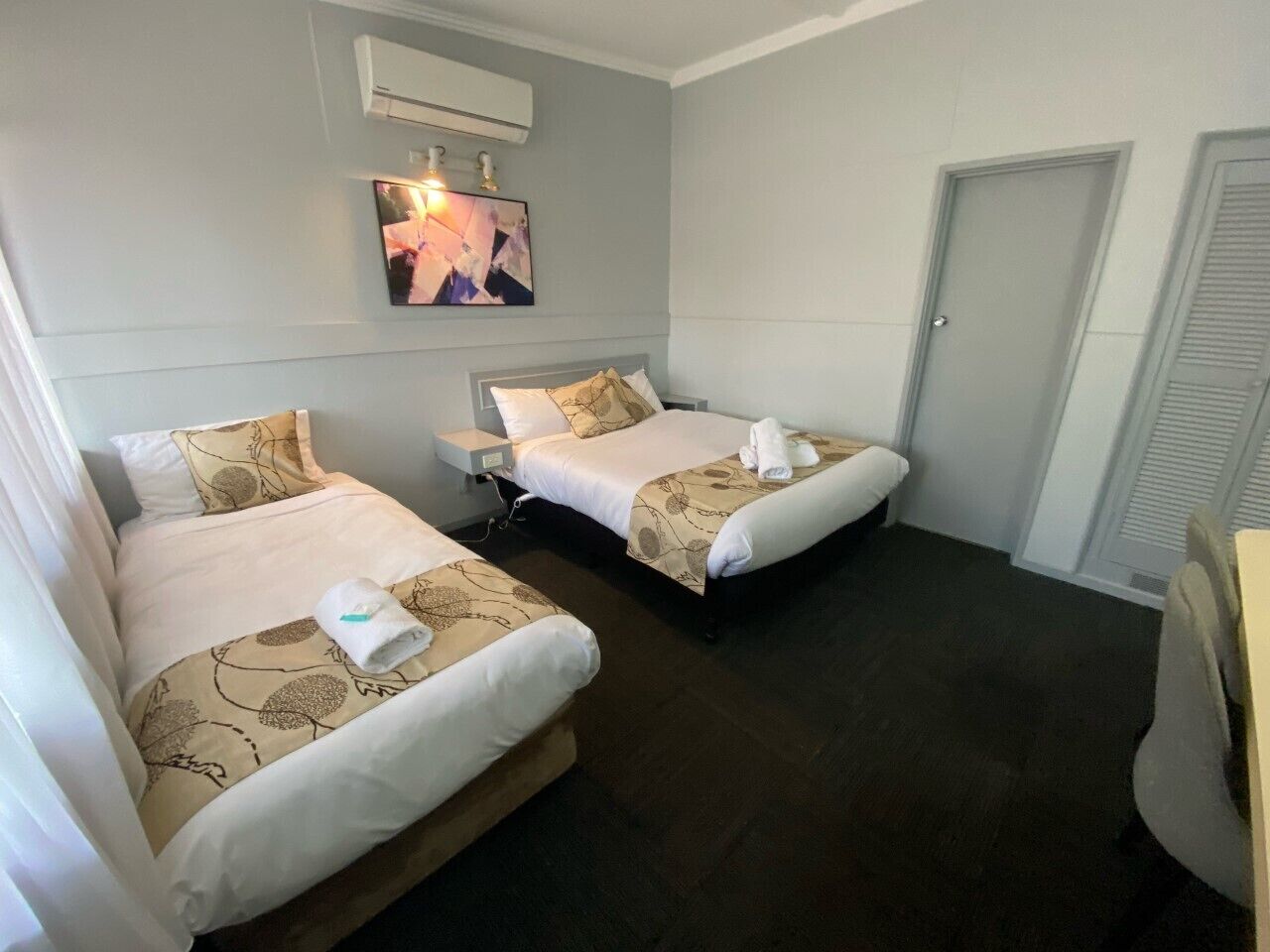 A hotel room with two beds, a bedside table, an air conditioning unit, and a door.