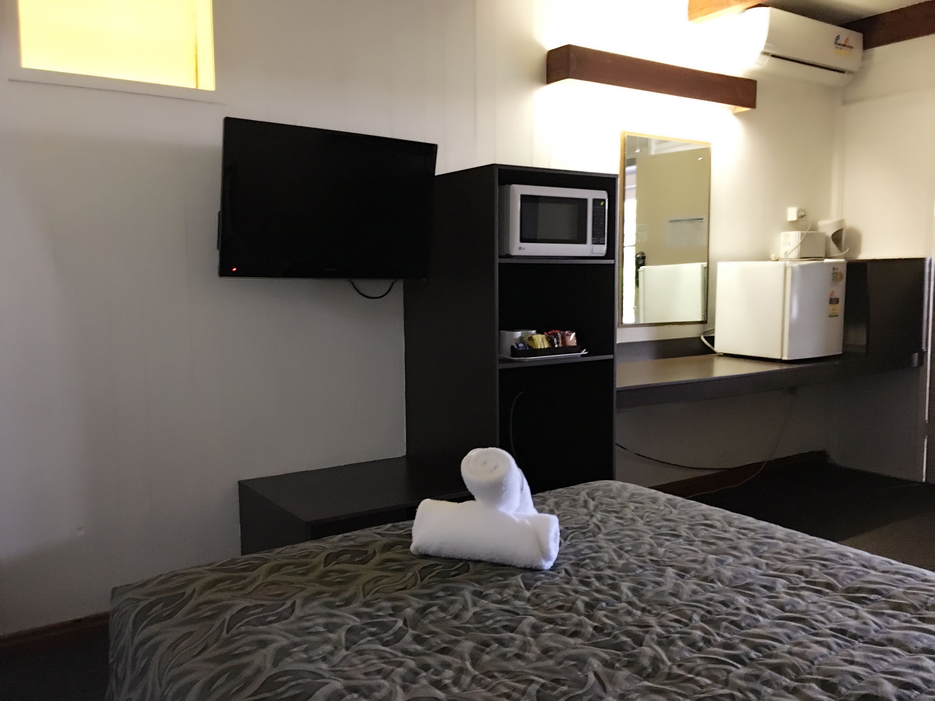 Une chambre d’hôtel équipée d’un lit, d’un téléviseur à écran plat fixé au mur, d’un four à micro-ondes, d’un réfrigérateur et d’une petite étagère contenant des articles de toilette.
