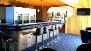 Una zona de bar con mostrador de acero inoxidable, taburetes y un televisor montado en la pared.