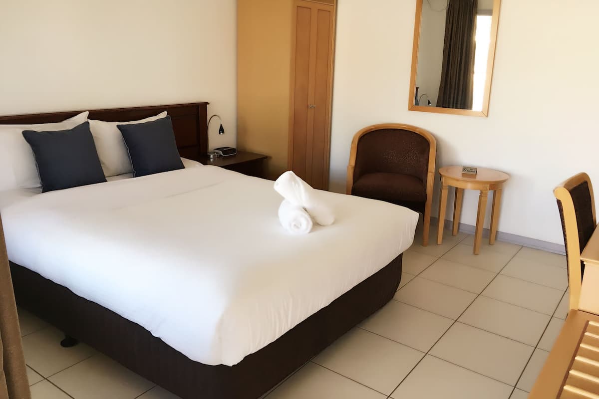 Una habitación de hotel con una cama grande, un armario, una silla, una mesita y un espejo en la pared.