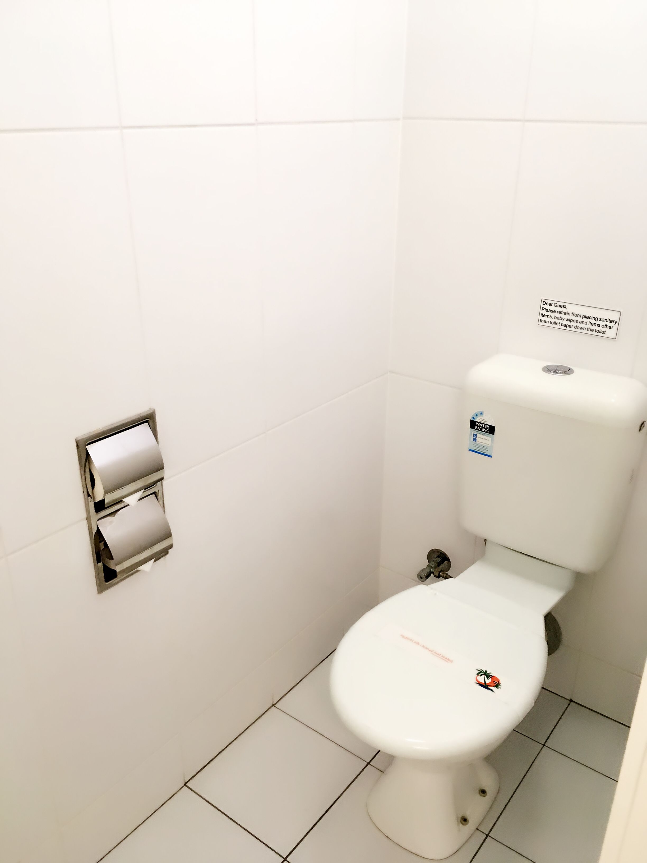 Eine weiße Toilette mit Spülhebel und einem an der Wand montierten Papierhandtuchspender.