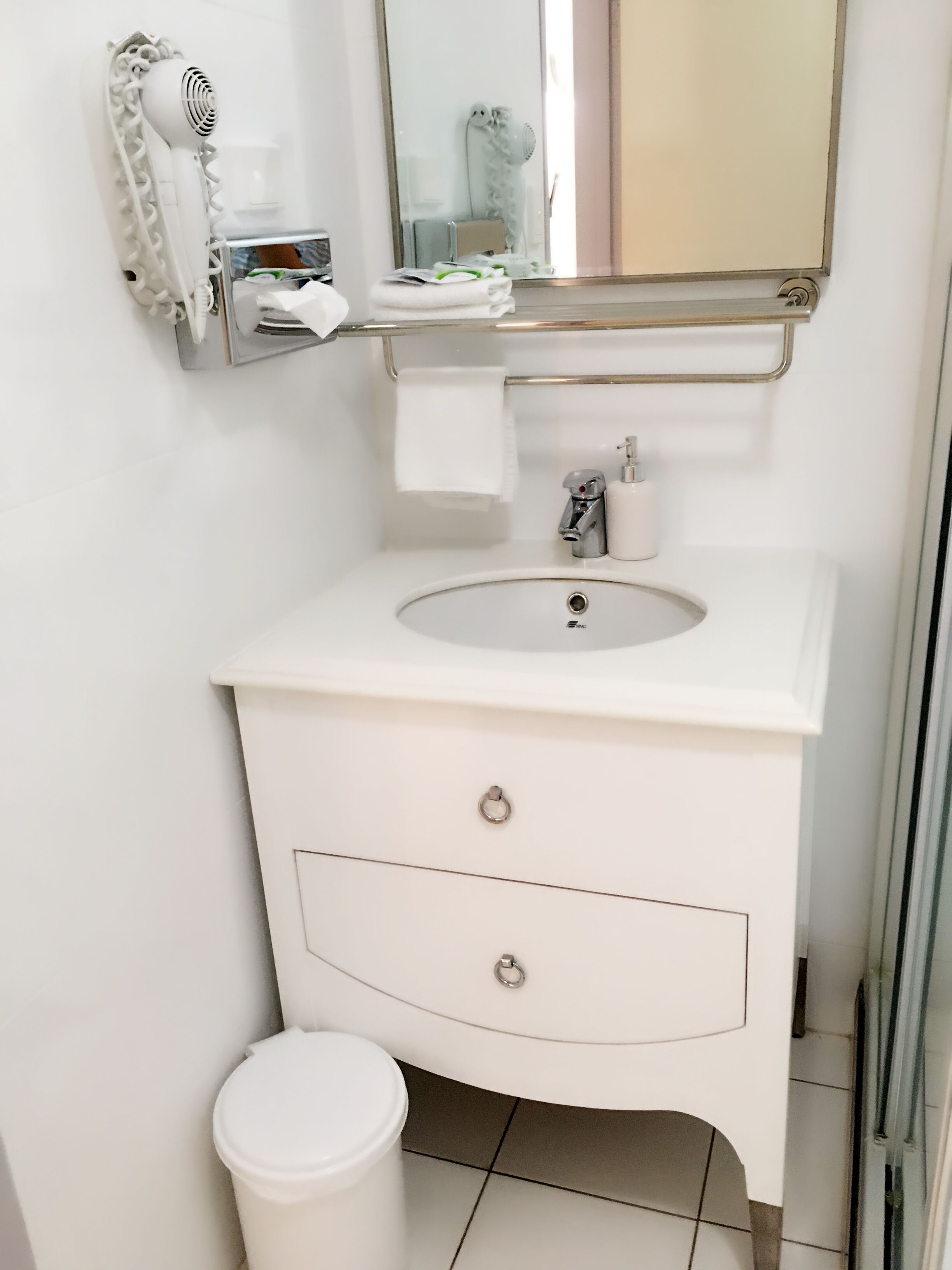 Un baño con lavamanos blanco, un espejo, toallero y un inodoro.