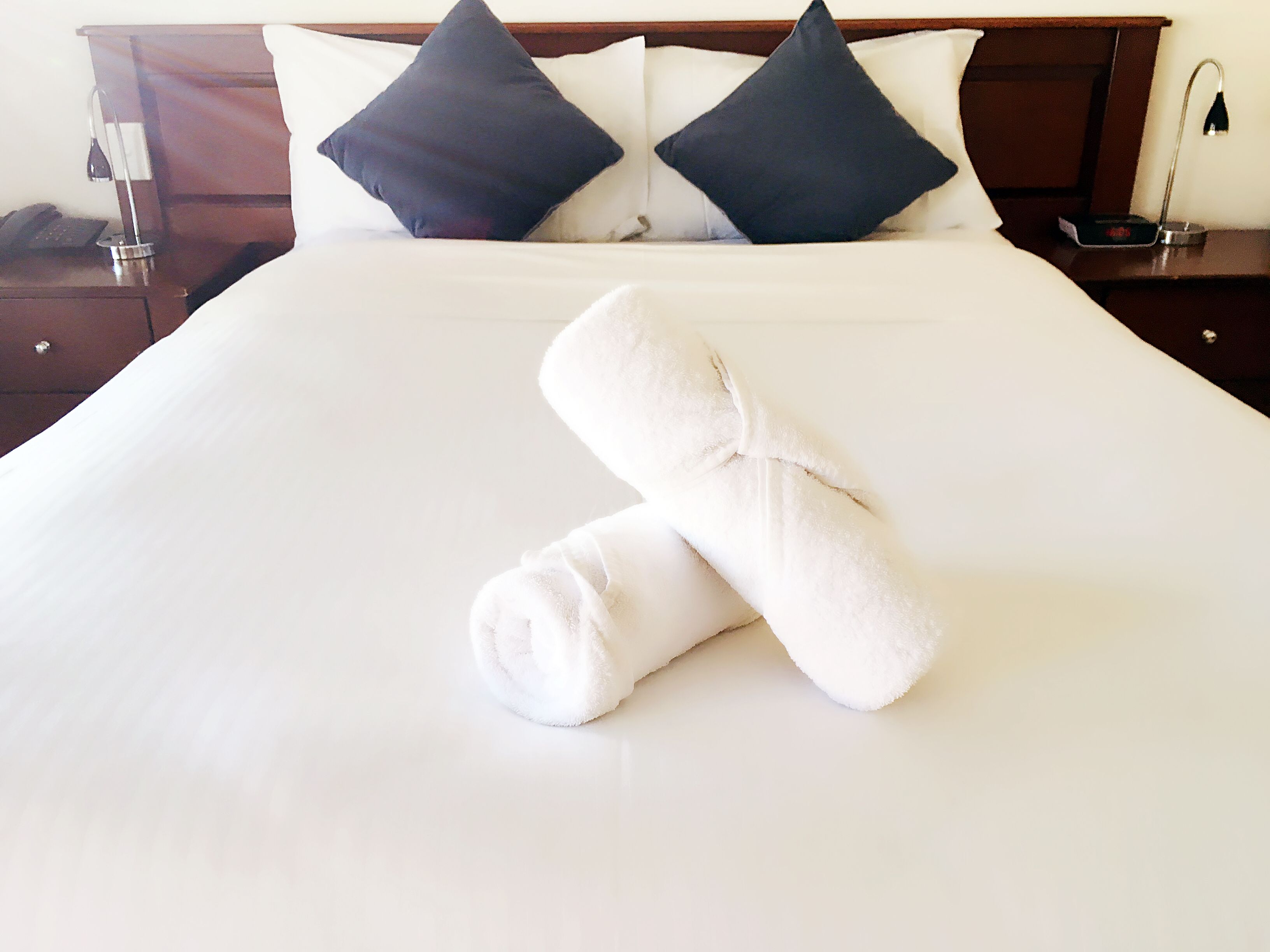 A neatly made bed with two pillows and a rolled towel.