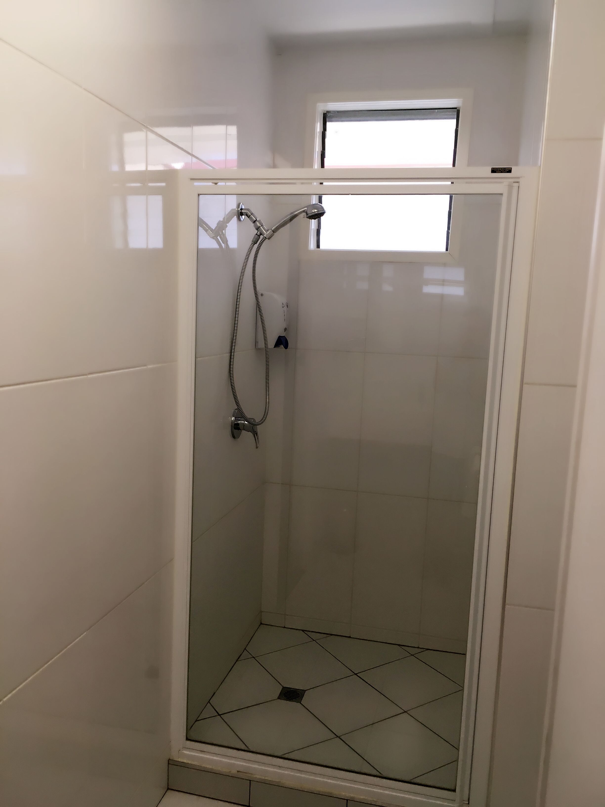 A small, enclosed shower area with a glass door, a handheld showerhead, and a window above the door.