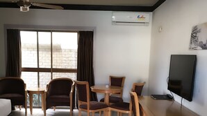Una habitación de hotel con zona de comedor, televisión y ventana con cortinas.