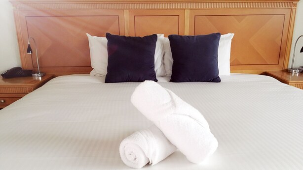 Una cama bien tendida con sábanas blancas y dos almohadas azul marino.