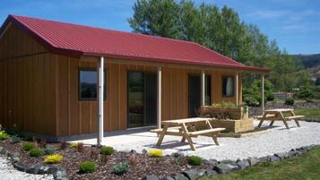 A wooden cabin with a red roof, a covered patio with picnic tables, and a gravel driveway.