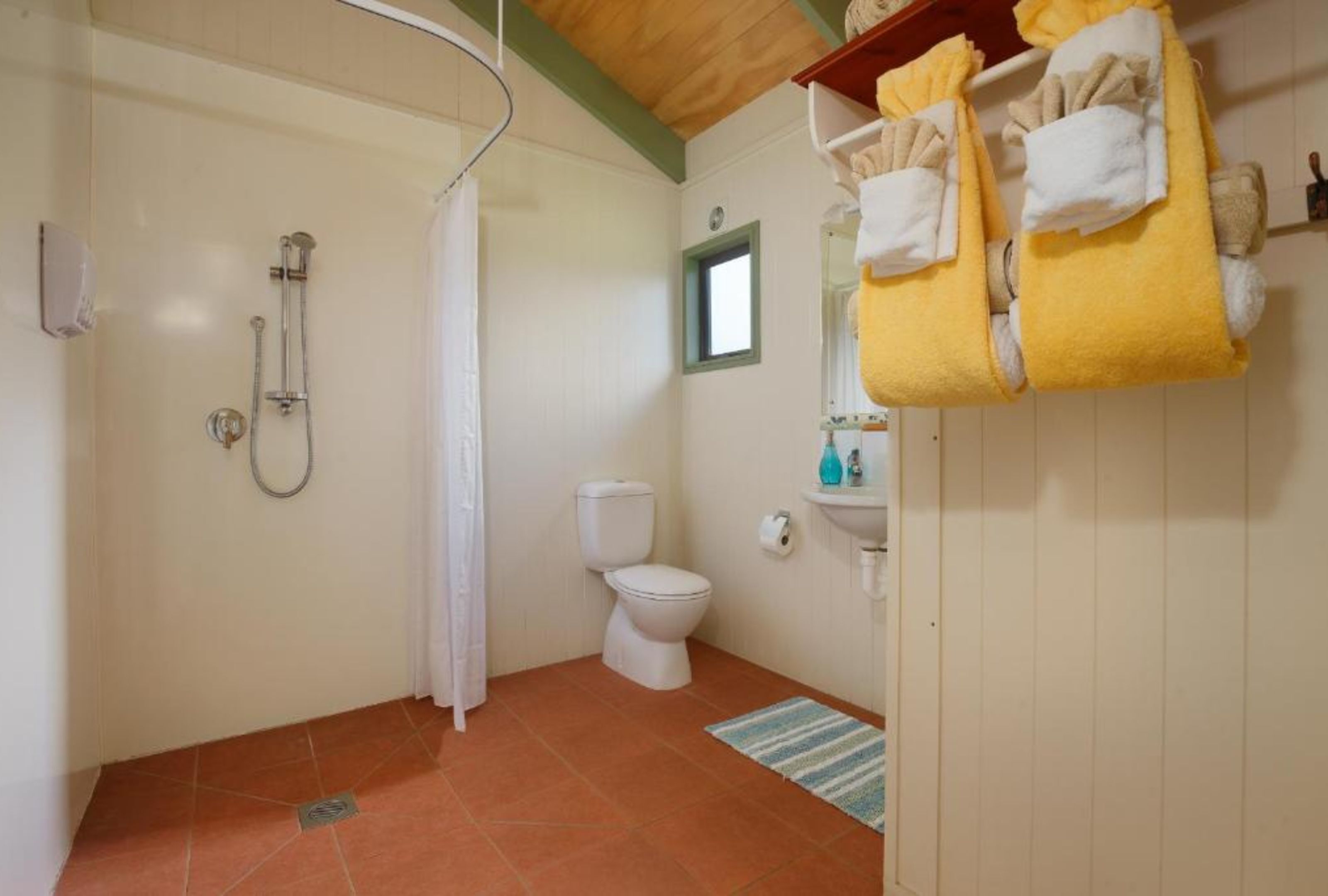 A bathroom with a shower, toilet, and sink. There are towels hanging on a rack.