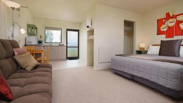 Een compacte hotelkamer met een bed, een slaapbank, een bureau met een computer en een kitchenette.