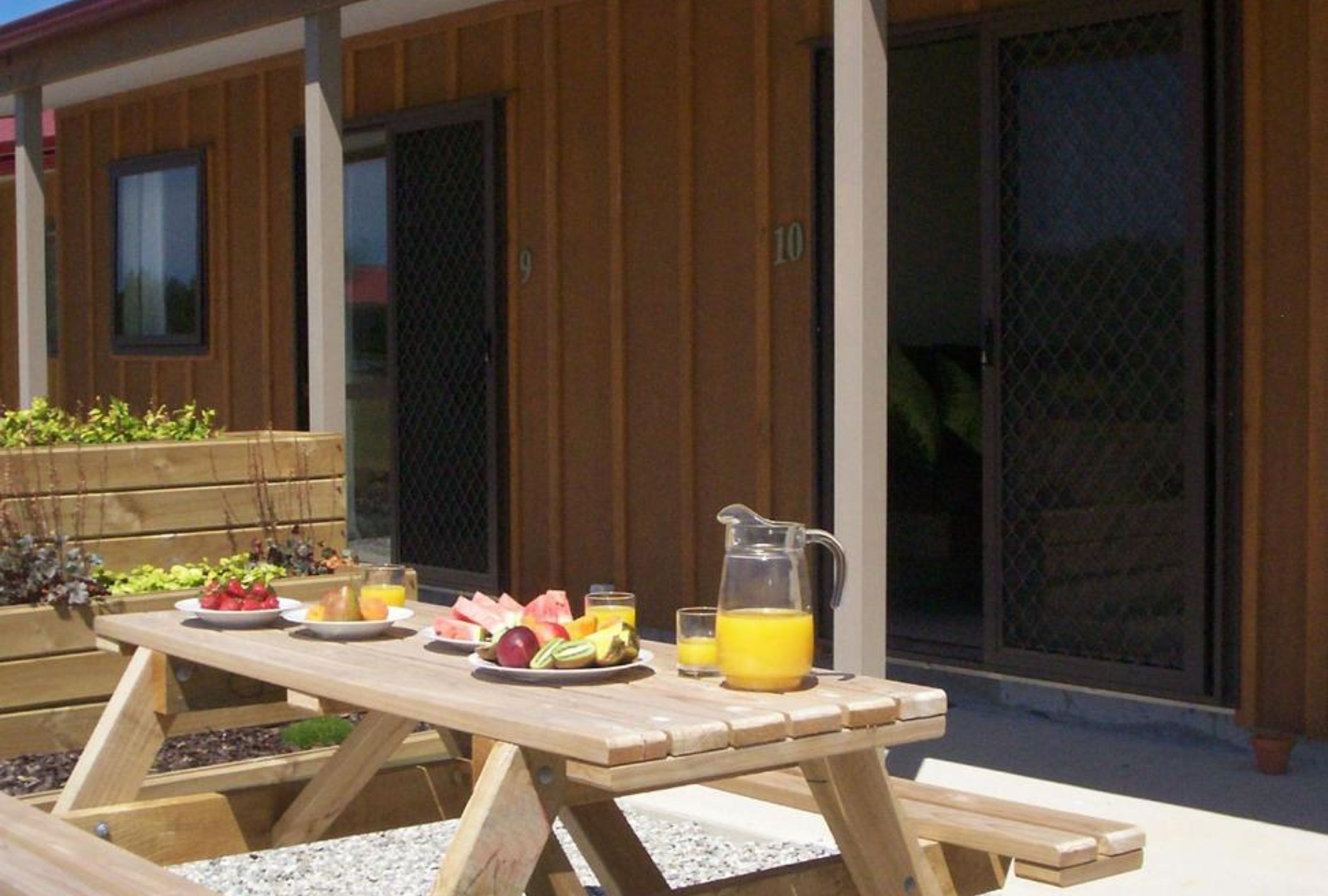 Een houten tuintafel gedekt met fruit, een karaf sinaasappelsap en een glas water.
