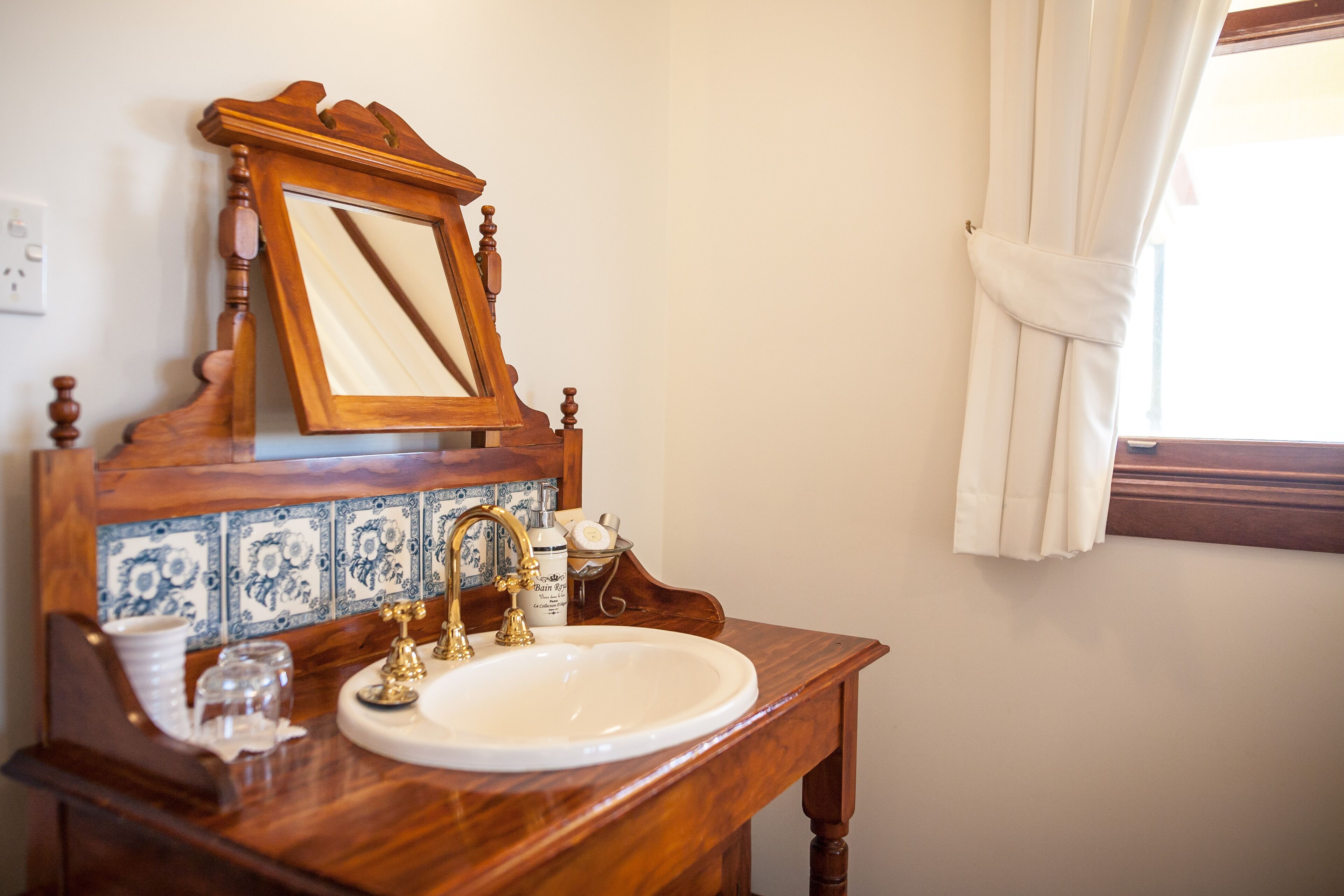 A bathroom with a wooden vanity, a white sink, a gold faucet, and a mirror with a wooden frame.
