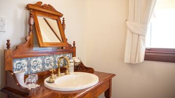 A bathroom with a wooden vanity, a white sink, a gold faucet, and a mirror with a wooden frame.