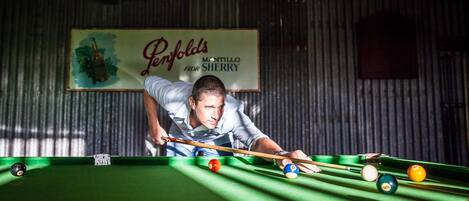 A billiards table with balls and cues, a man leaning over the table, and a sign in the background.