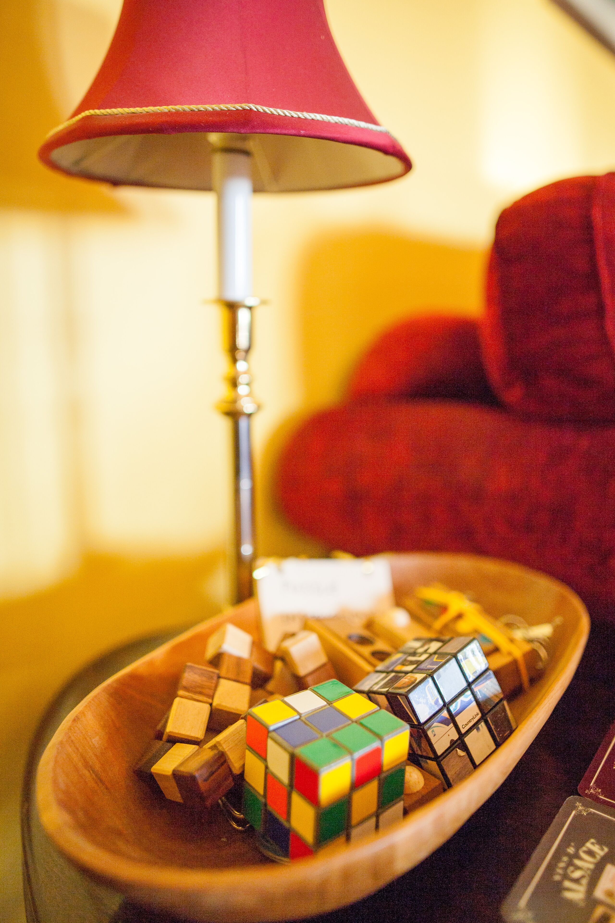 A wooden bowl containing various Rubik's cubes on a table with a red lamp in the background.