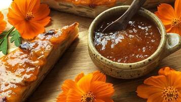 A glazed pork chop with a side of sauce, garnished with flowers on a wooden surface.