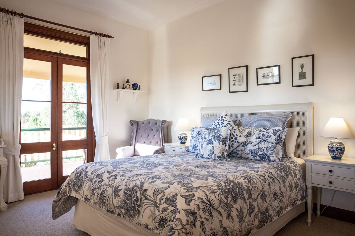 A bedroom with a large bed, a chair, a nightstand, and a door leading to an outdoor area.