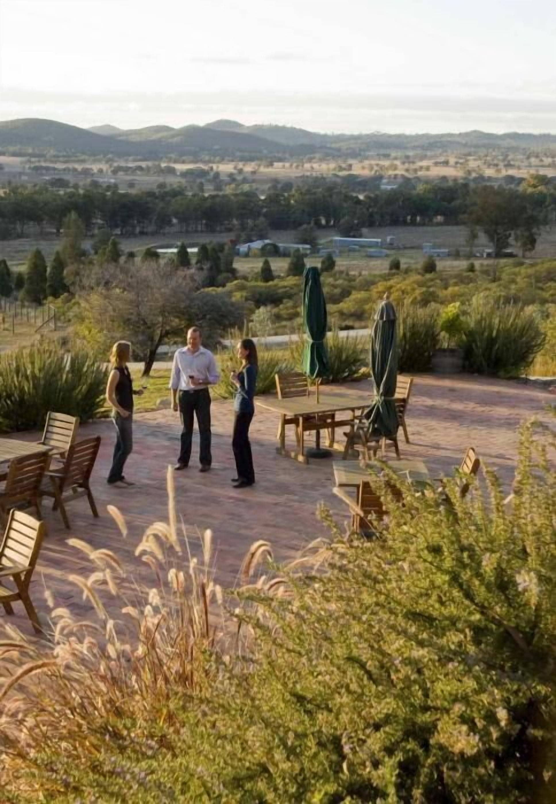 Un patio al aire libre con mesa y sillas, rodeado de follaje y colinas al fondo.