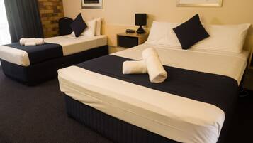 A hotel room with two beds, each with white linens and black headboards. There is a small bedside table with a lamp and a clock on one side.