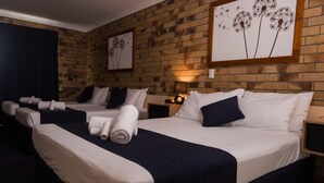 A hotel room with two beds, dark blue bedding, white pillows, and a brick wall. - Lancaster Court Motel (Annerley)