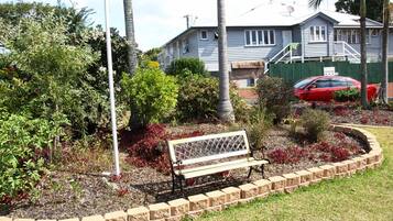 Uma área residencial com um banco em um jardim ajardinado, um carro vermelho estacionado em frente a uma casa e um poste de luz.