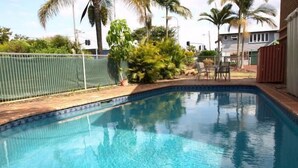 A clear blue swimming pool with a tiled edge, surrounded by a fenced area and palm trees. - Lancaster Court Motel (Annerley)