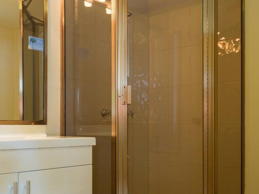 A bathroom with a glass-enclosed shower, a white vanity with a mirror, and a tiled floor.