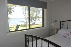 Un dormitorio con cama, mesita de noche, lámpara y ventana con vista al lago.