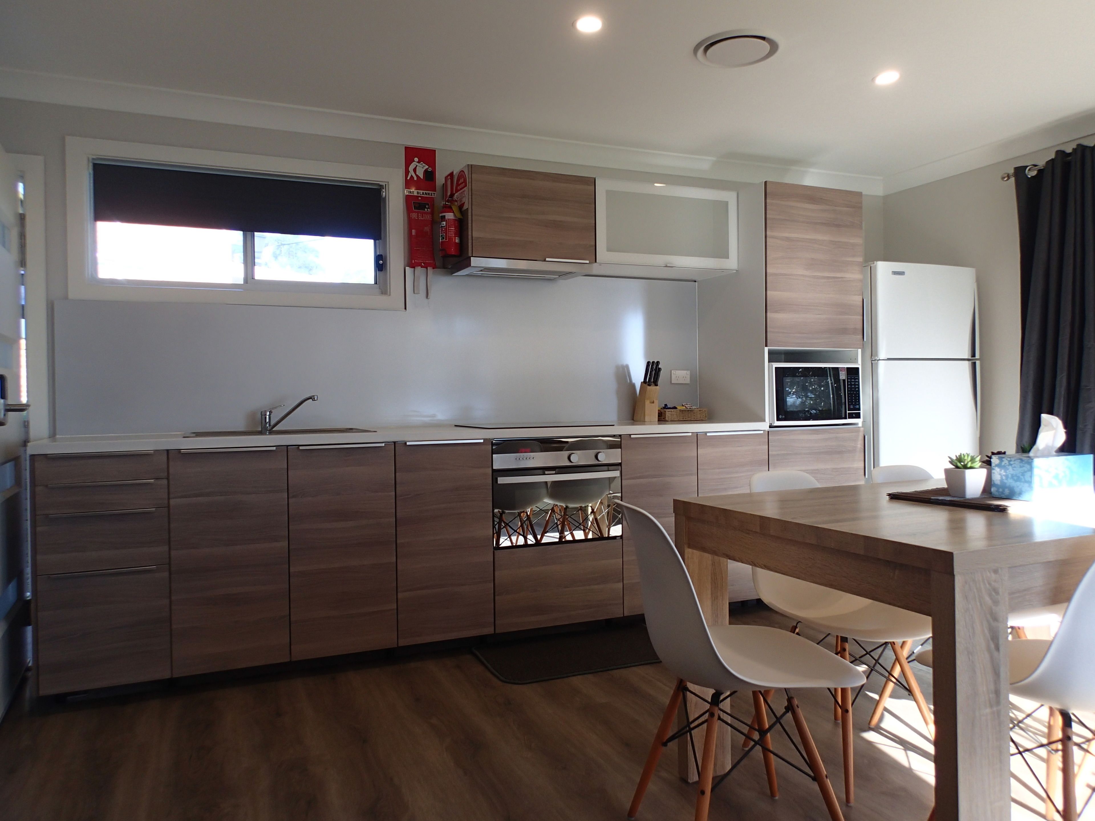 A modern kitchen with wooden cabinets, a built-in oven, a microwave, and a dining area with a table and chairs.