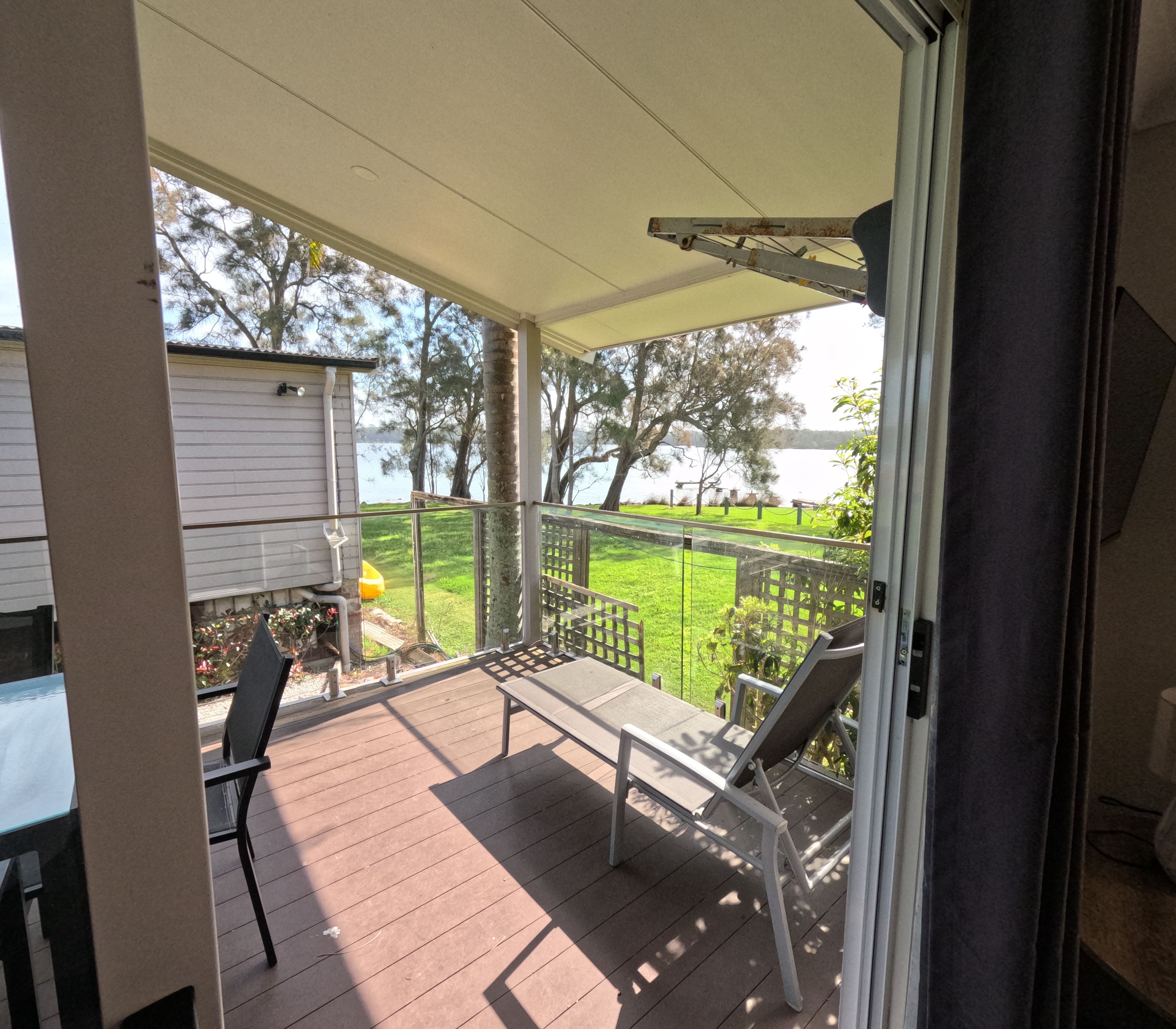A covered outdoor area with a view of a lake, a wooden deck, and a chair.