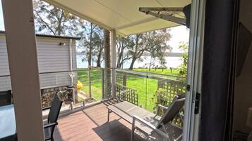 A covered outdoor area with a view of a lake, a wooden deck, and a chair.