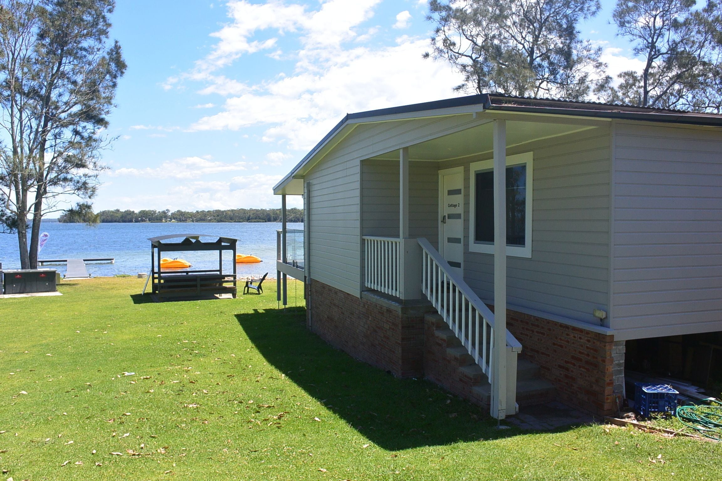 A small cabin with a porch, a covered seating area, and a view of a lake.