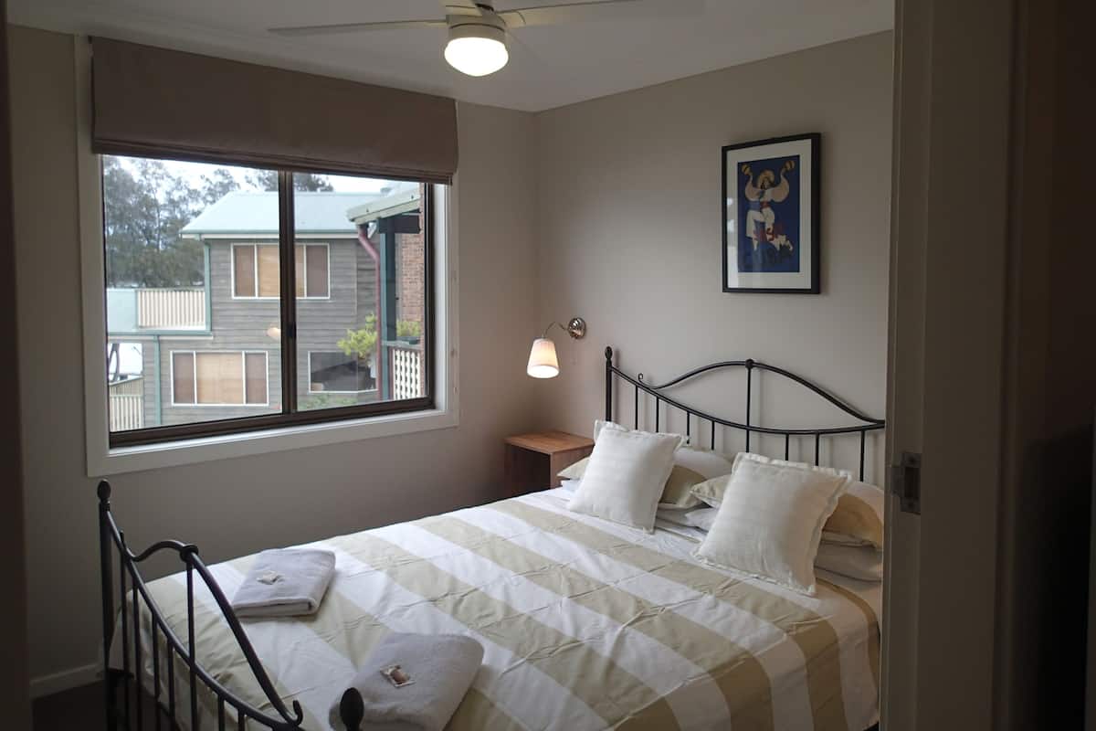 Ein Schlafzimmer mit einem Bett, einem Deckenventilator, einem Fenster und einem gerahmten Bild an der Wand.
