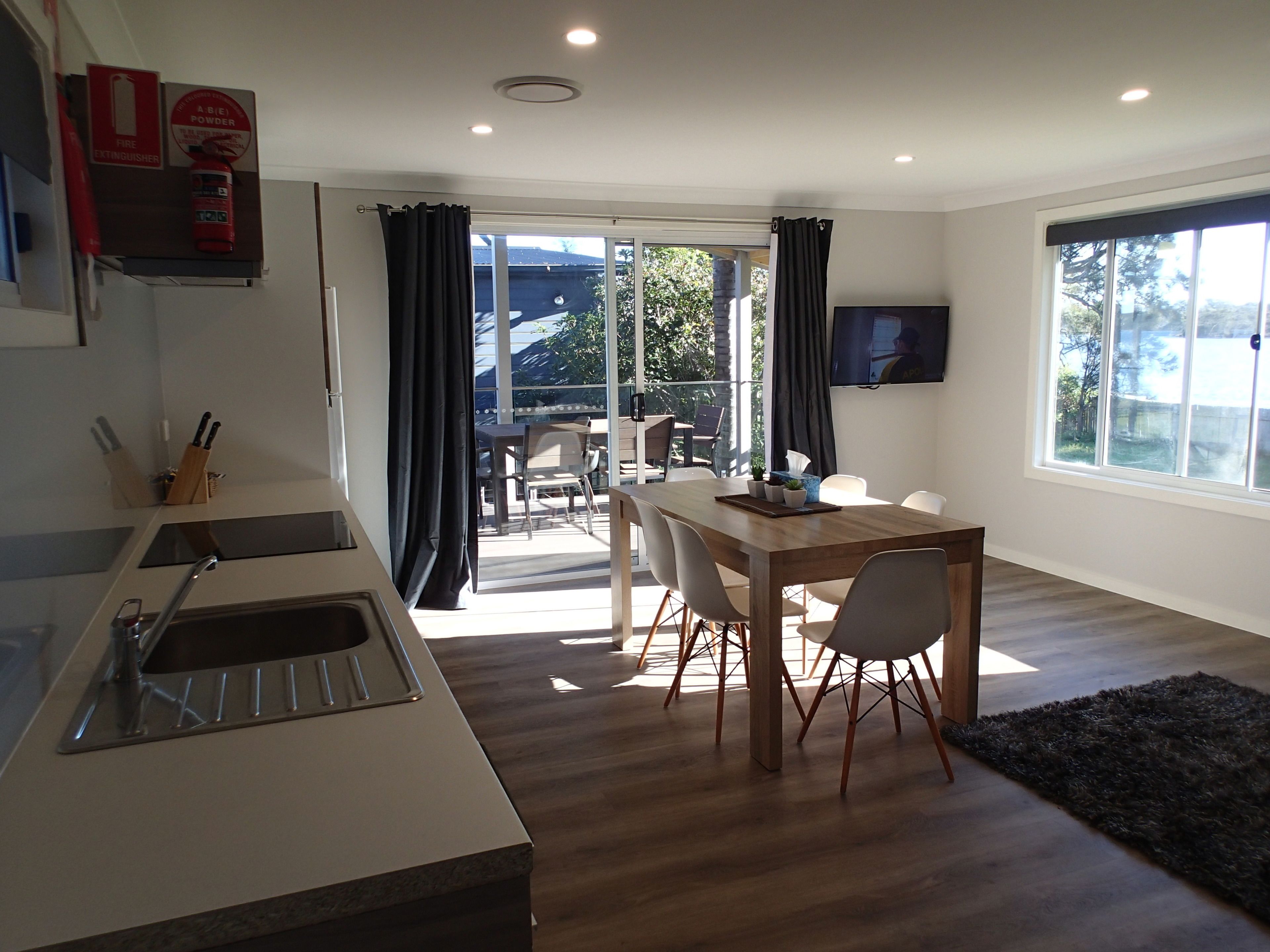 A modern kitchen with a sink, a dining area with a table and chairs, and a large window with curtains.