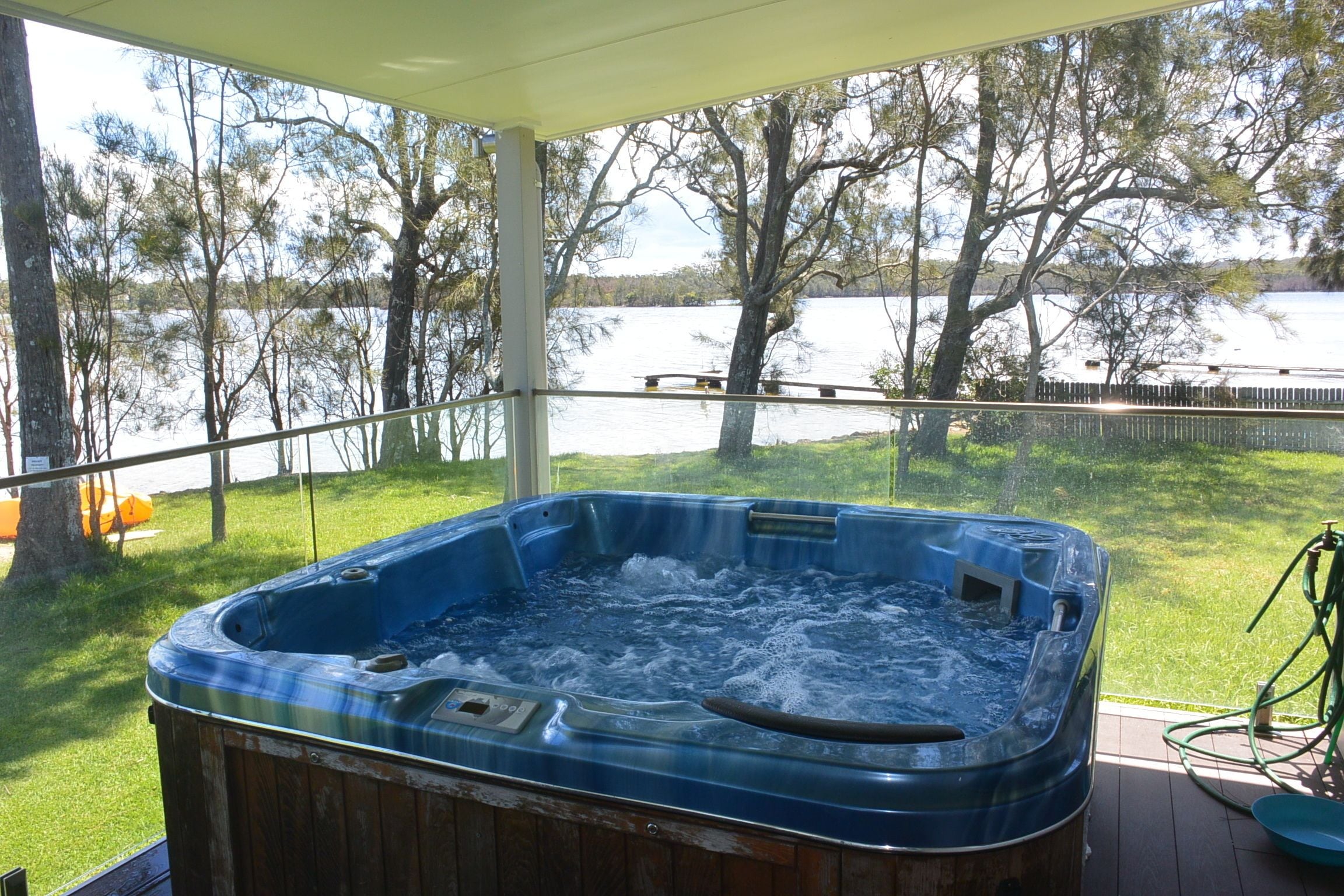 A hot tub on a wooden deck with a view of a lake and trees.