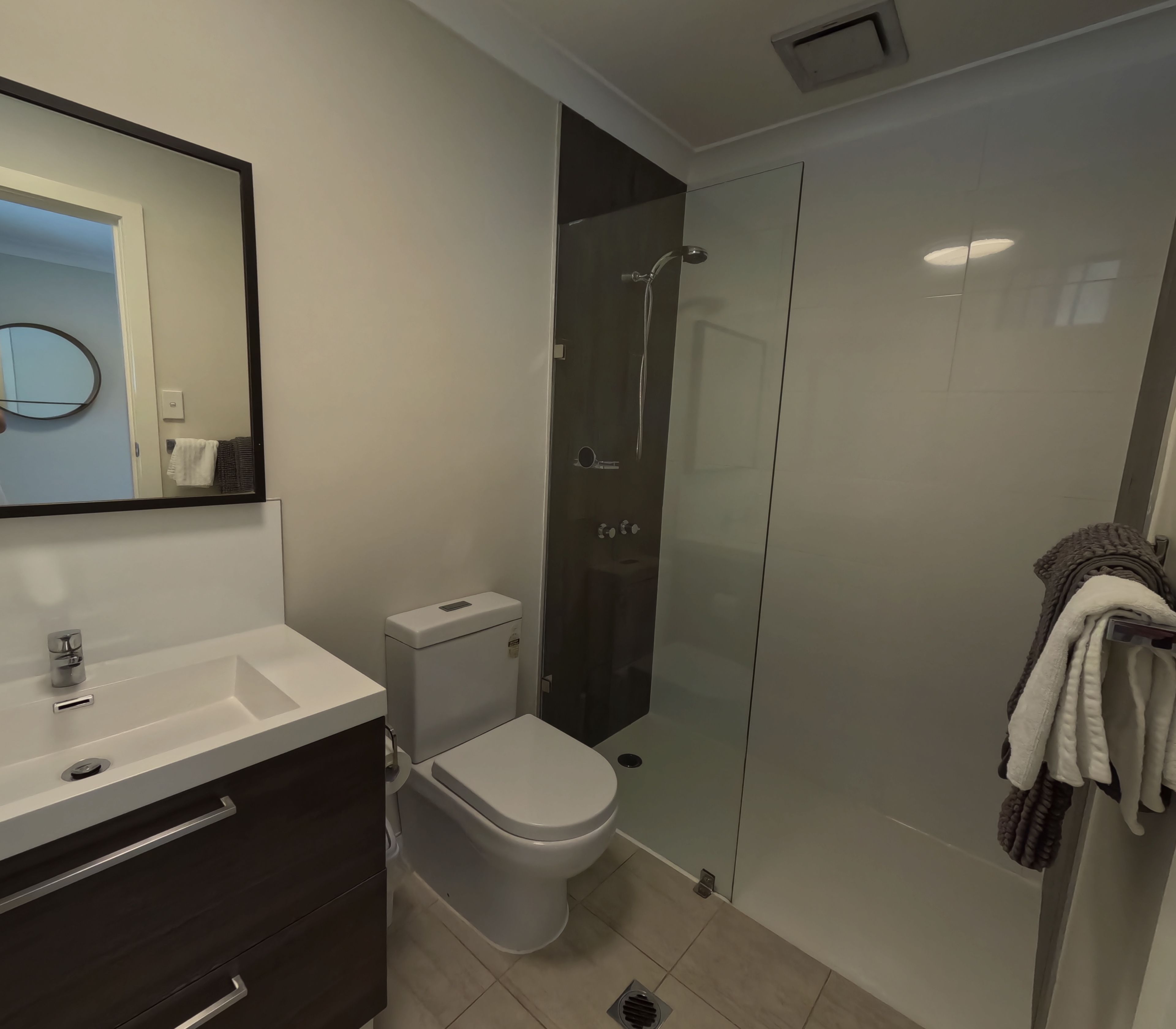 Une salle de bain moderne avec une douche à parois de verre, des toilettes blanches, un meuble-lavabo avec un miroir et un porte-serviettes.